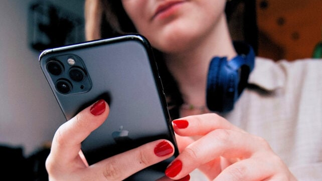 Low angle view of a person with red painted fingernails, holding a black smartphone while looking down at it