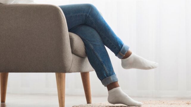 Black woman using smartphone sitting with crossed legs on chair