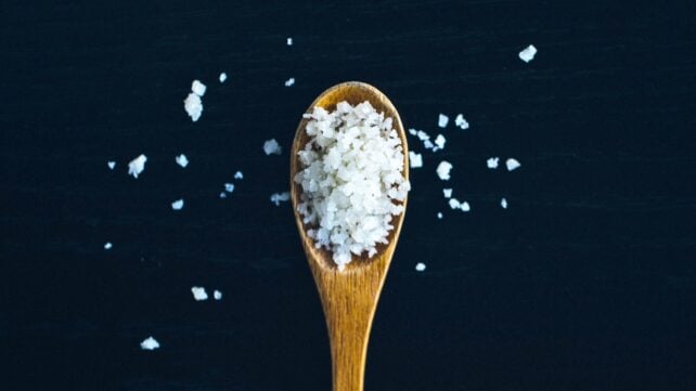 Aerial view of wooden spoon filled with salt, on a high-contrast black background