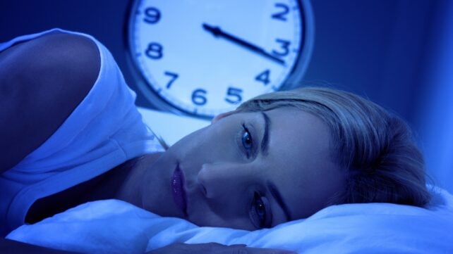 Woman awake in bed, with a clock showing 3:15 am in the background