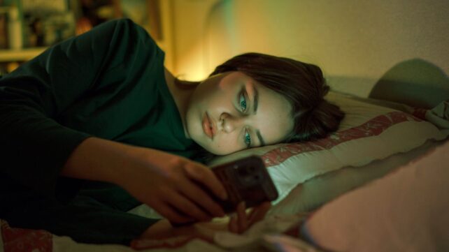 A teenager lying in bed and looking at a phone screen