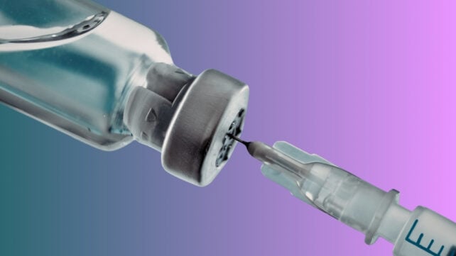 Close up image of an upturned vial with a medical syringe drawing liquid from it