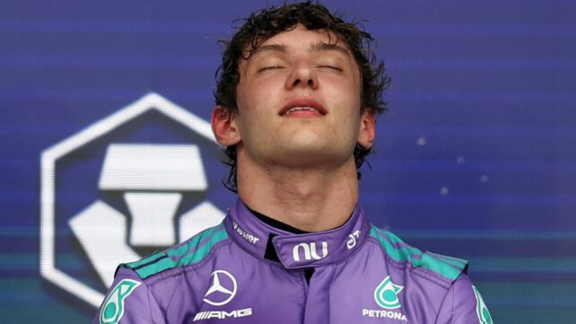 Formula 1 driver in a purple racing suit tilts his head back with his eyes closed after a race