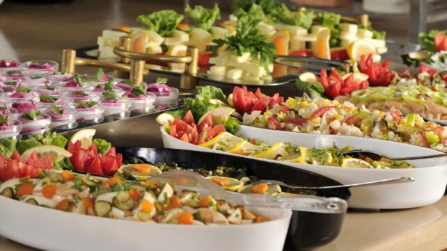Buffet spread with trays of salads, vegetables, cheese, eggs, and shared serving utensils