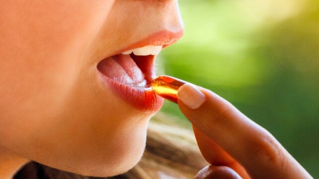 A hand about to place a supplement into a mouth, highly-contrasted by a sunlit background