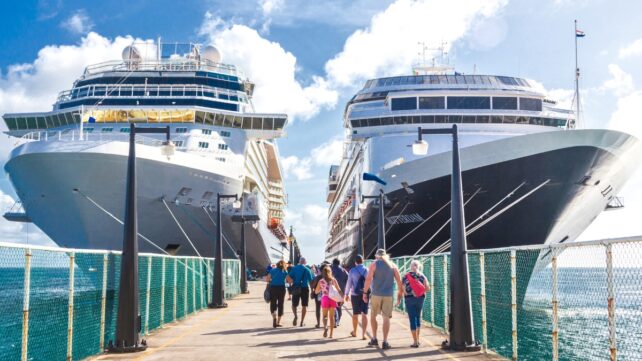 Passengers walking along a pier to board two large cruise ships docked side by side