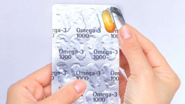 Omega-3 supplements in blister pack, with hand removing one