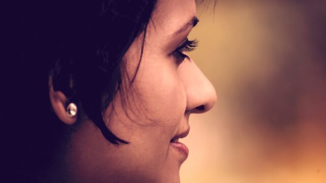 Close-up side profile of a woman with dark hair against a warm, blurred background.