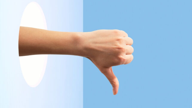 A hand poking through a hole in blue space, showing thumbs down
