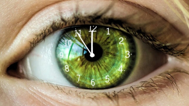 Close-up of a green human eye with clock numbers and hands overlaid on the iris, symbolizing biological aging and the passage of time.