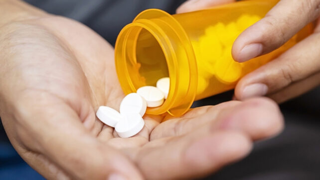 Man pouring white pills into hand from orange prescription bottle