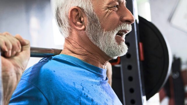 Older man in a blue top is lifting weights for longevity