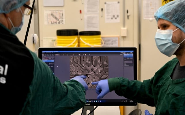 Two scientists in lab gear point at a microscope image of cortical and hippocampal cells displayed on a computer screen.
