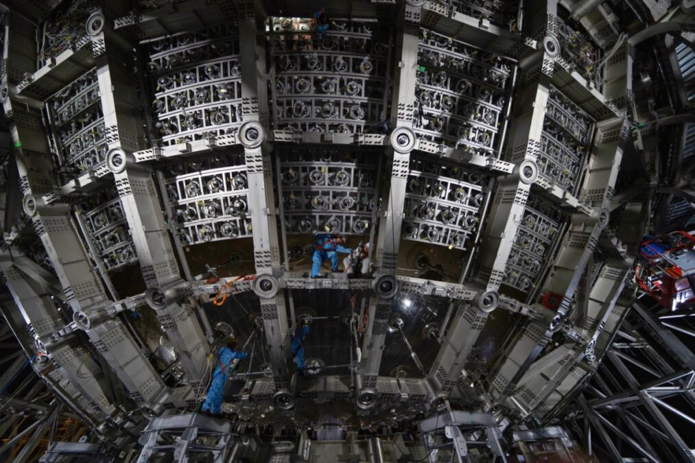 Workers In Blue Protective Suits Install Components Inside The Large Spherical JUNO Detector 1013x675