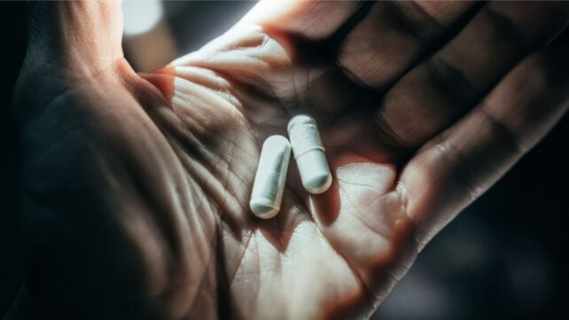 hand holding two white capsules that look like probiotic supplements