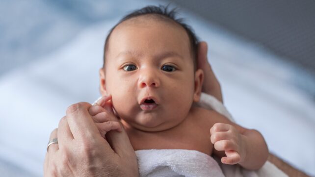 Close up photo of a one week old baby boy with dark hair and eyes open, mixed race, Asian and Caucasian