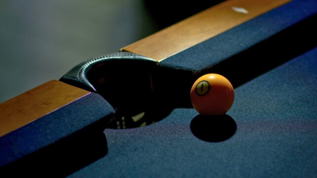 Close-up of a billiard ball near a pocket on a pool table