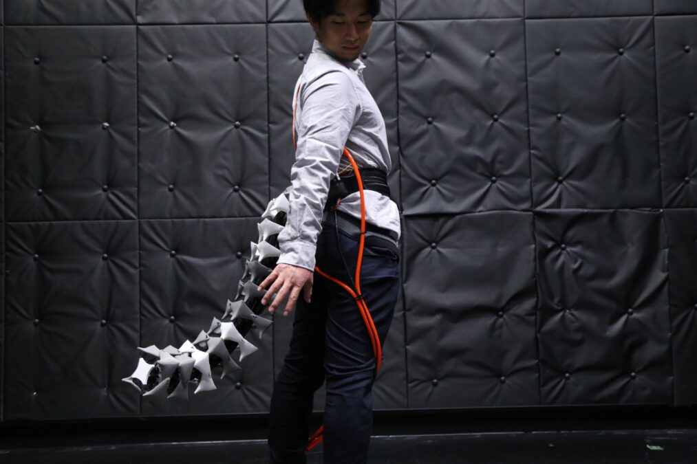 Person wearing the segmented Arque robotic tail attached to a waist harness in a laboratory.