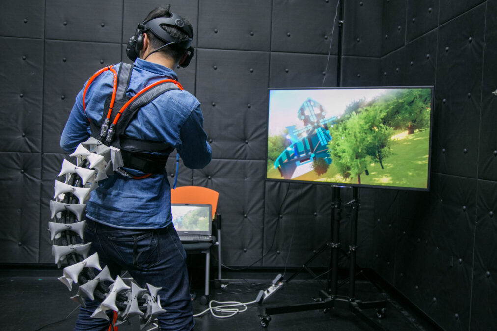Person wearing a virtual reality headset with the Arque robotic tail attached to their back.