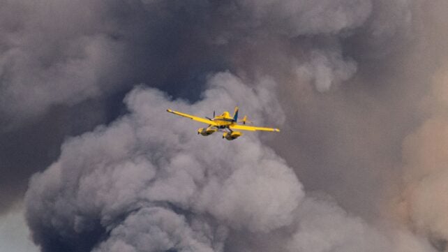 Dramatic scene of a yellow airplane flying through dense smoke, possibly from a wildfire