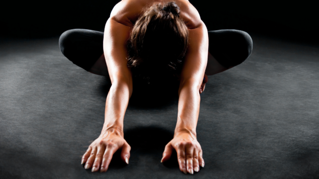 woman stretching forward in yoga pose, on high contrast background